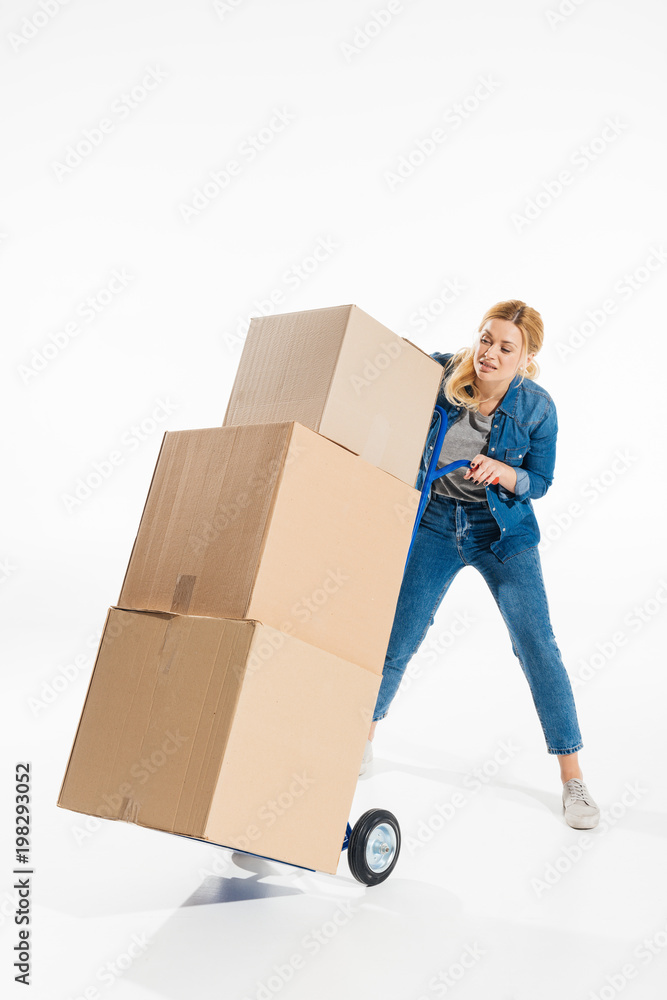 Attractive woman struggling with delivery cart loaded with boxes isolated on white Attractive woman struggling with delivery cart loaded with boxes isolated on white