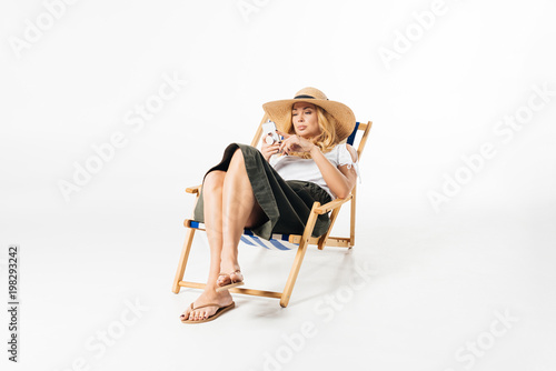 Blonde woman using smartphone and resting in deck chair on white background © LIGHTFIELD STUDIOS