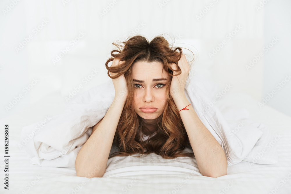 Sad confused young lady lies in bed