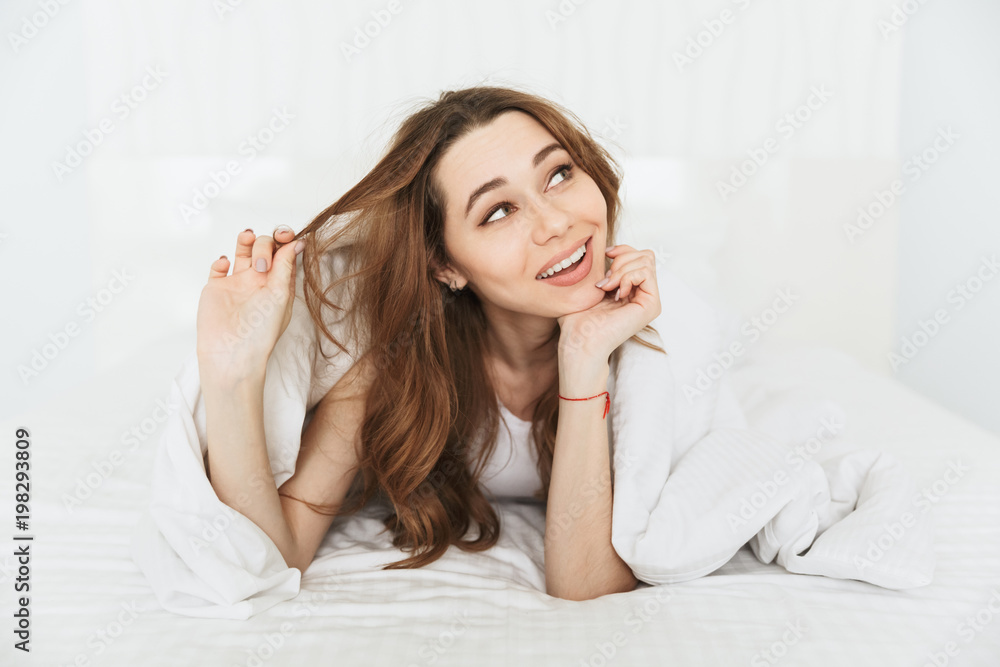 ICute young woman lies in bed indoors at home ICute young woman lies in bed indoors at home