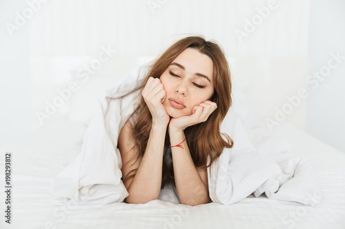 Sleepy young lady lies in bed indoors at home