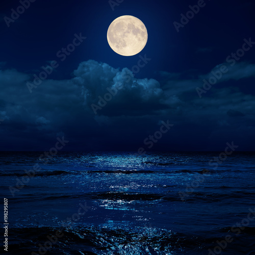 full moon in night over clouds and sea with reflections