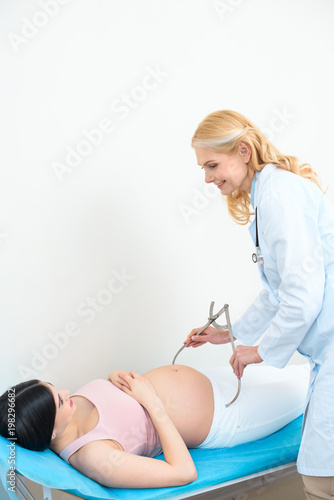 mature obstetrician gynecologist measuring pelvis size of pregnant woman with pelvimeter photo