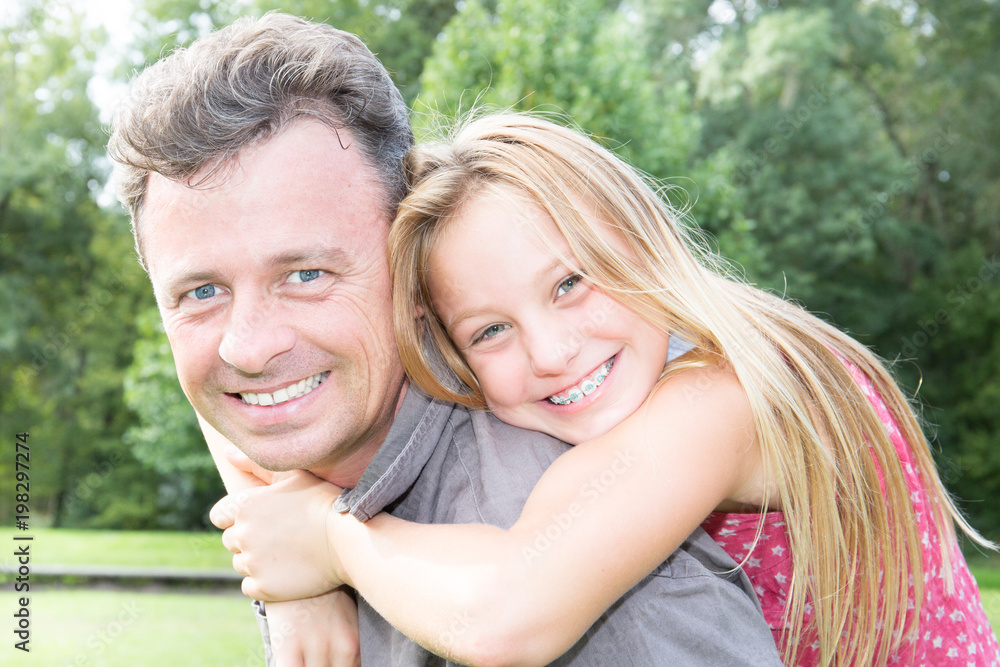 father hugging with her teen daughter outdoor in nature on sunny day piggyback
