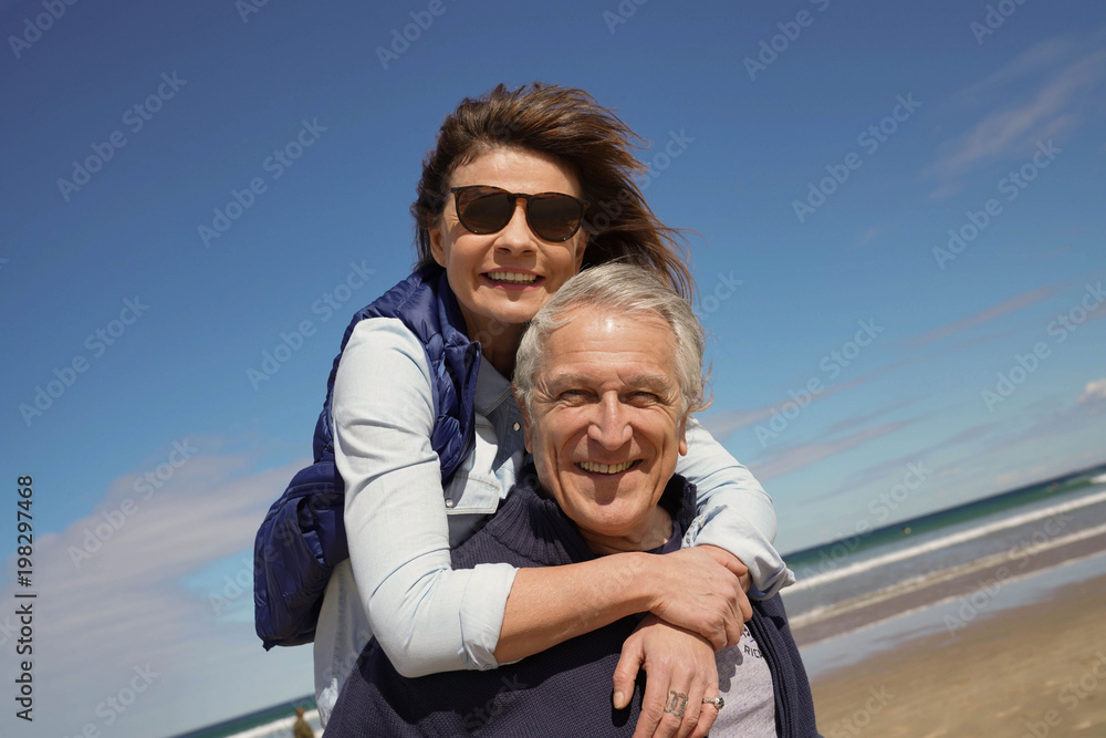 Senior man giving piggyback ride to woman at the beach