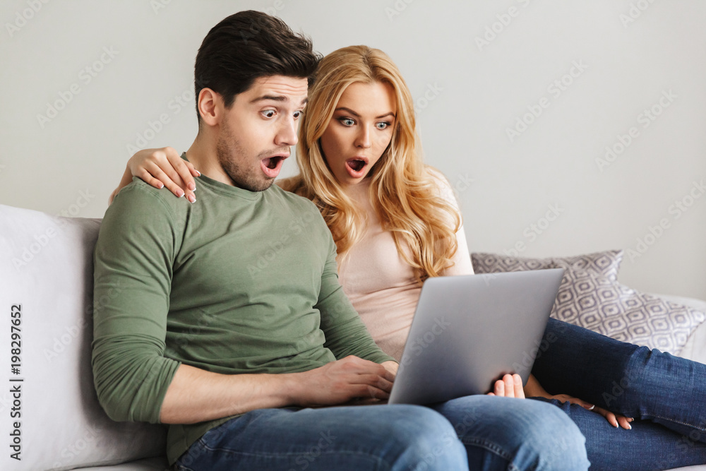 Shocked young loving couple sitting on sofa Shocked young loving couple sitting on sofa