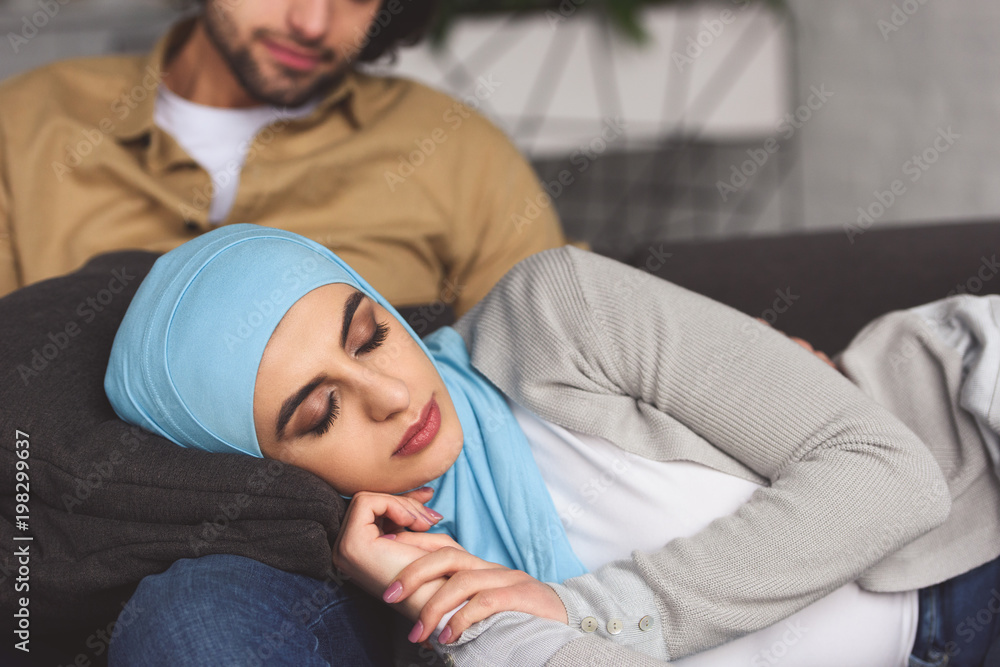 muslim girlfriend in hijab sleeping on boyfriends legs at home Stock