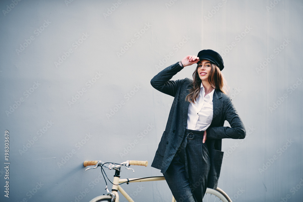 Woman posing in front of wall yellow bicycle behind her.. Hand holding hat. Woman posing in front of wall yellow bicycle behind her.. Hand holding hat.
