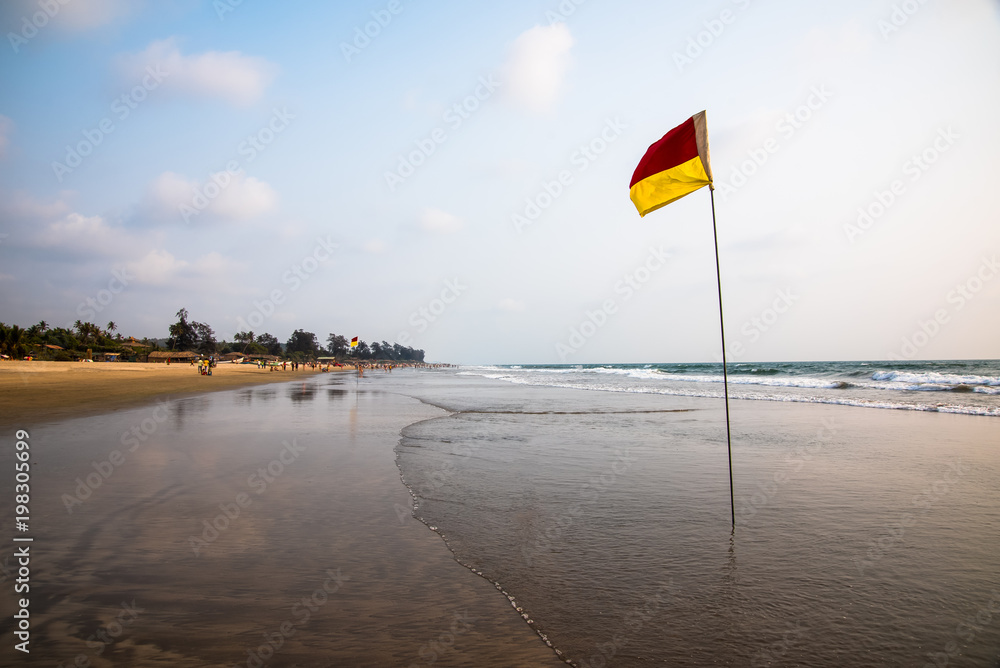 Red and yellow safety flag on long sandy beach