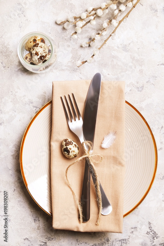 Easter table setting composition: quail eggs, candle, wilflowers, pussy willow on plate w/ napkin, white stucco plaster texture background. Close up, top view, copy space, greeting, template.