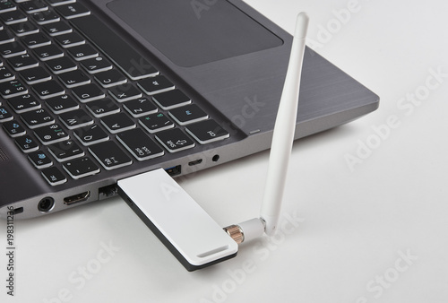 Silver laptop with USB modem plugged in with an antenna, on a white table
