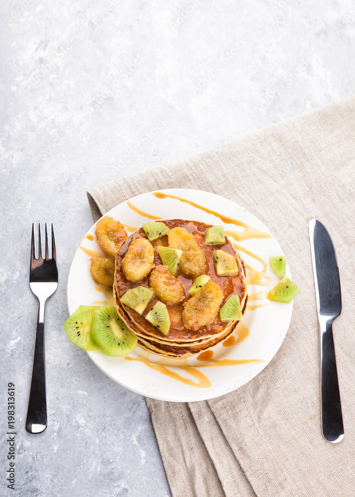 Homemade breakfast on a marble grey table. Stack of pancakes with a grilled bananas and a caramel, kiwi slices. Healthy breakfast concept, flat lay, top view Homemade breakfast on a marble grey table. Stack of pancakes with a grilled bananas and a caramel, kiwi slices. Healthy breakfast concept, flat lay, top view