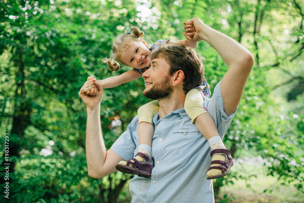 Obraz premium Father and daughter playing piggyback at outdoor garden park. Cute little blonde girl and man with a beard having fun
