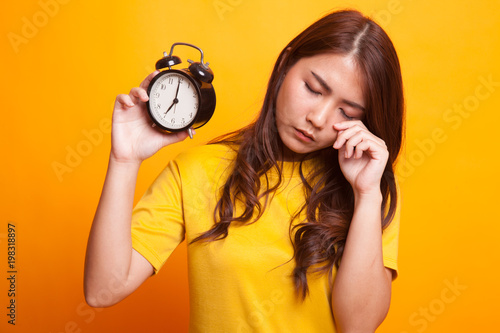 Sleepy young Asian woman with a clock in the morning in yellow dress