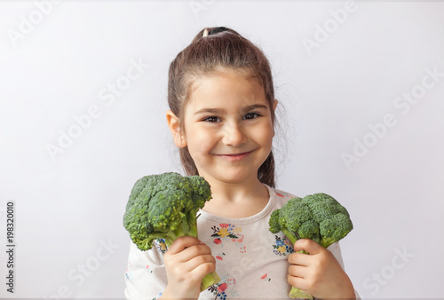 Happy little girl eating fresh vegetables ,fruits and drinkind fresh juice. A portrait on a white background. Healthy teeth.