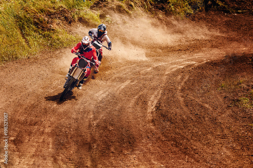 Fototapeta Naklejka Na Ścianę i Meble -  Racer on dirtbike motorcycle jumps and takes off over track, in background opponent is catching up. Concept primacy, rivalry, competition, extreme