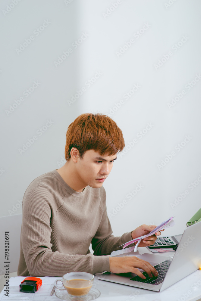 Unhappy man paying bills on his laptop in living room Unhappy man paying bills on his laptop in living room