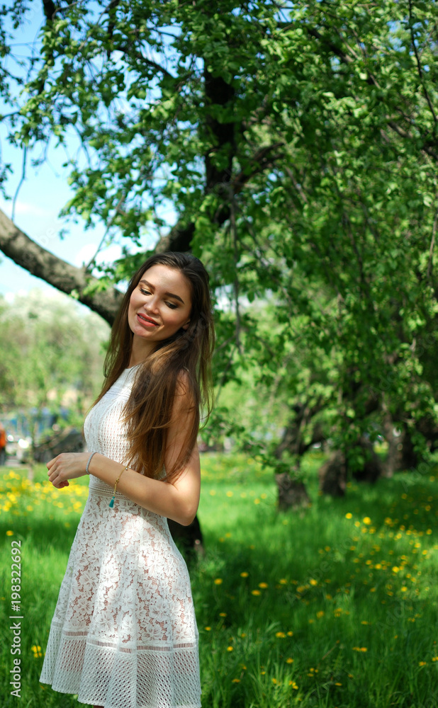 Beautiful smiling brunette girl standing in the alley in the summer background. Beautiful smiling brunette girl standing in the alley in the summer background.