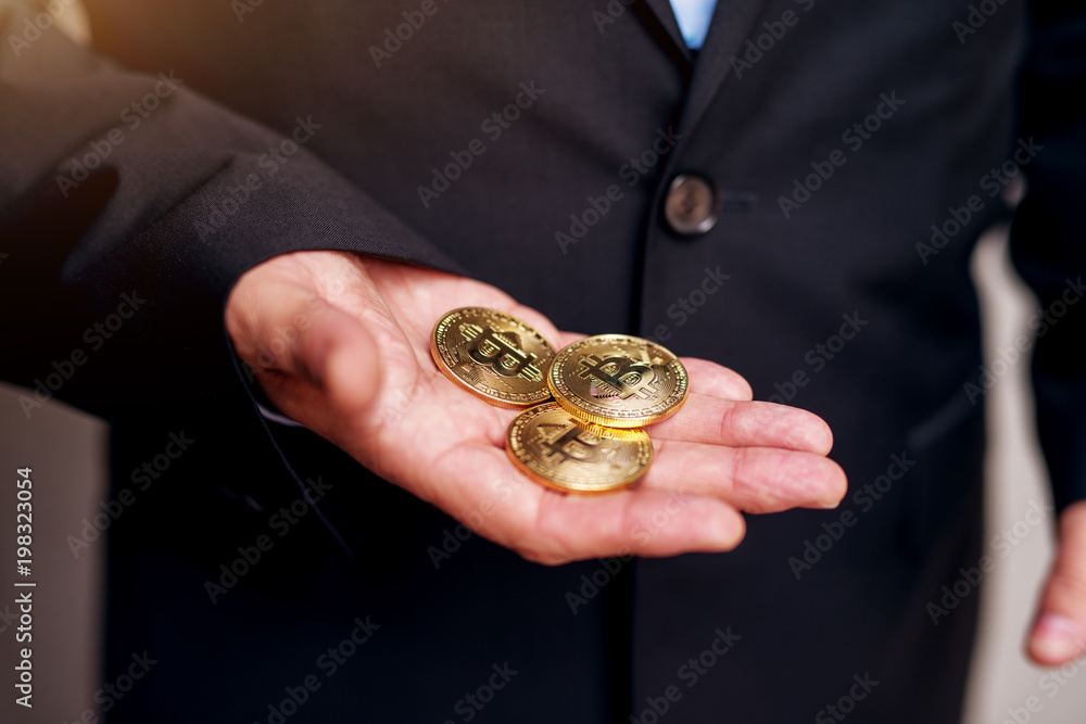 Close up of a mature businessman in suit hands holding three bitcoins.