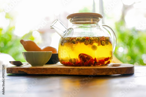 Chinese green tea in a transparent teapot is on a wooden table. In the background, a bright sunny morning illuminates everything around. Side view with copy space