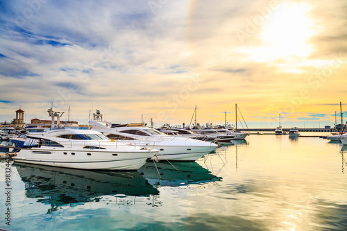 Luxury yachts at sunset. Marine dock of modern motor and sailing boats in sunshine, blue water sea, rainbow with sun. Travel and fashionable vacation.