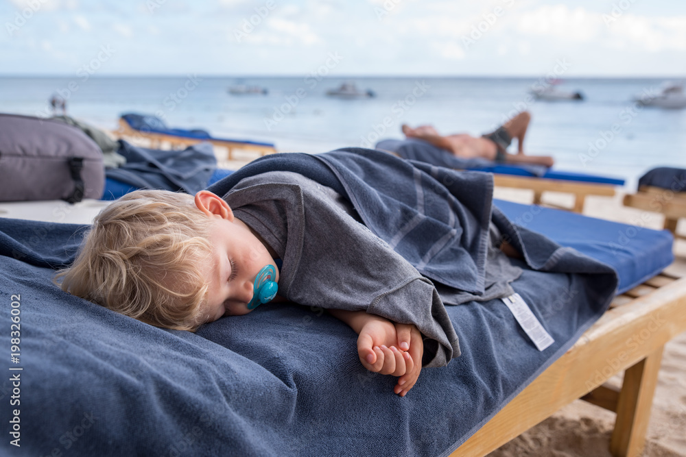 Fototapeta premium beautiful baby boy sleeping on deckchairs at the beach during the day