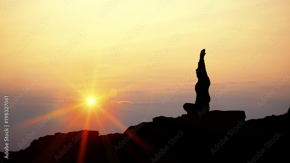 Silhouette young woman practicing yoga on the top of mountain in golden sunset