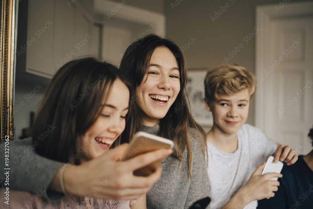 Close-up of cheerful friends with smart phones at home Close-up of cheerful friends with smart phones at home
