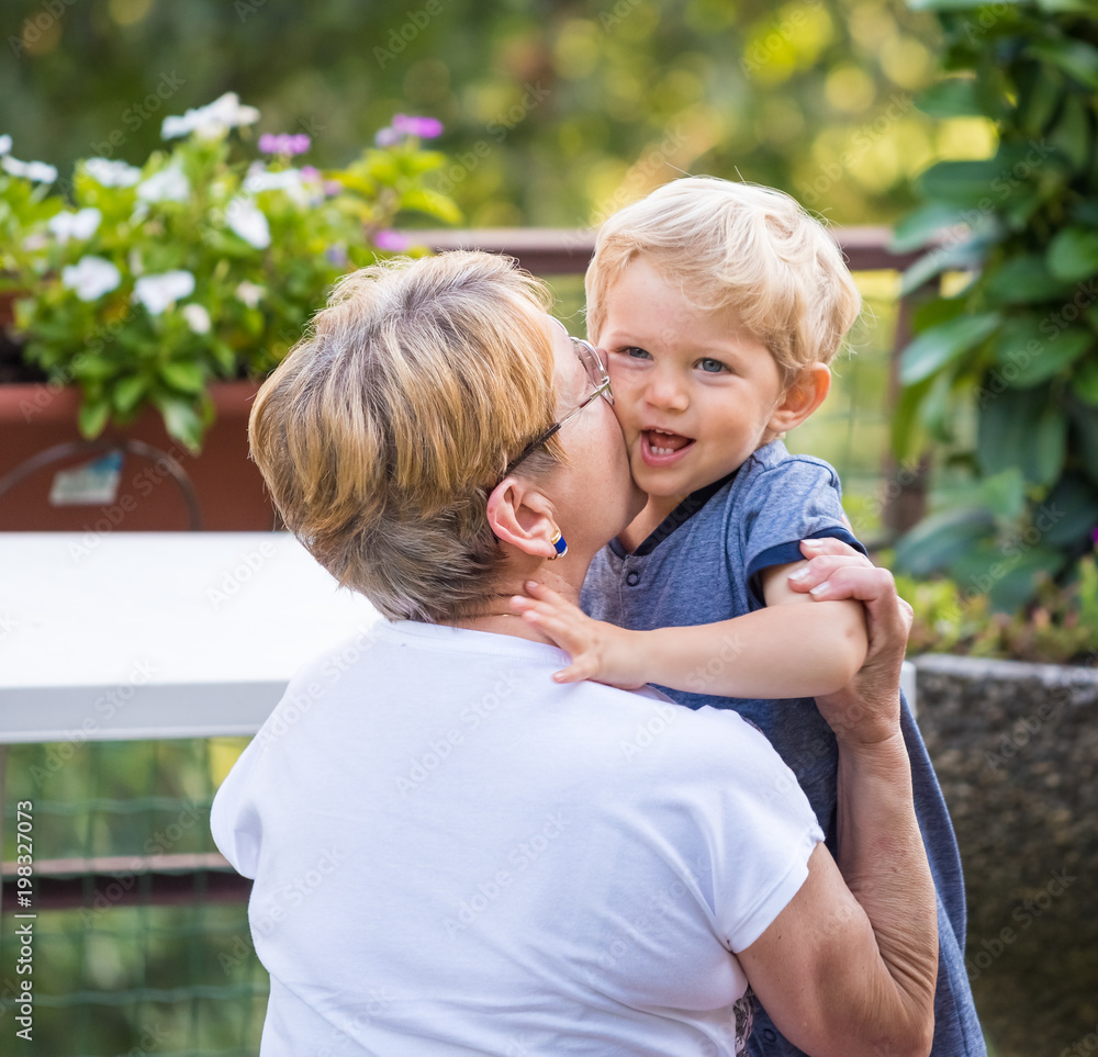 Grandmother hugs and gently kisses her grandchild in garden, natural light. Grandmother hugs and gently kisses her grandchild in garden, natural light.