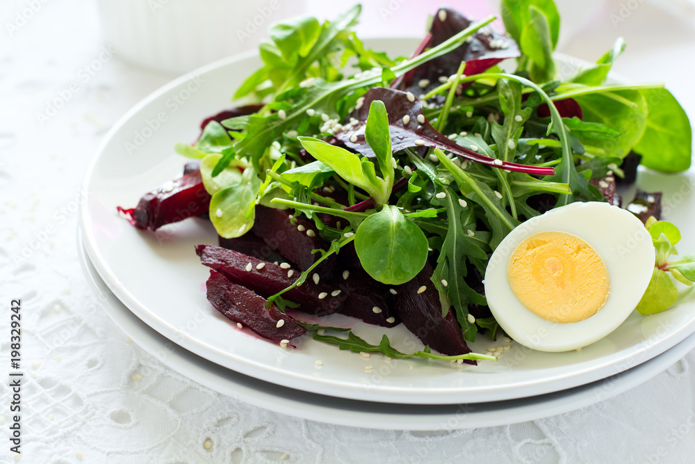 Fresh salad with beetroot, mix leaves, olive oil, egg and sesame seeds on white table cloth Fresh salad with beetroot, mix leaves, olive oil, egg and sesame seeds on white table cloth