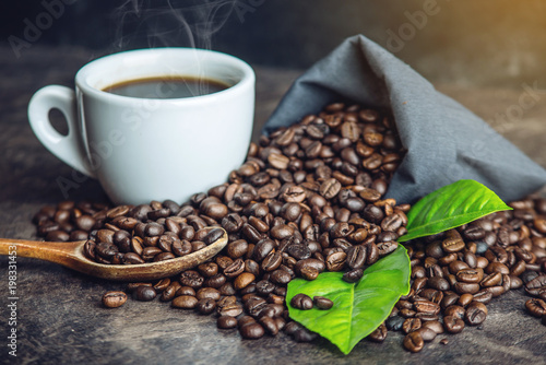 White black espresso Cup with pile of coffee beans and green leaves in bag on dark background