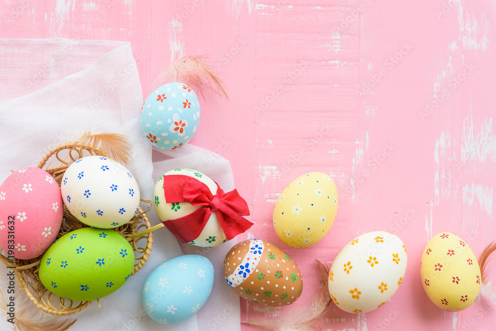 Happy easter! Colorful of Easter eggs tied with red ribbon in nest with paper star, flower and Feather on pastel color bright pink and white wooden background.