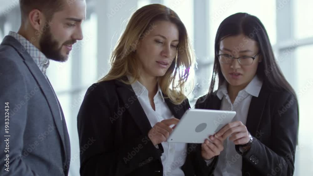 Medium shot of businesswomen and businessman in formal clothing looking at tablet and discussing work Medium shot of businesswomen and businessman in formal clothing looking at tablet and discussing work