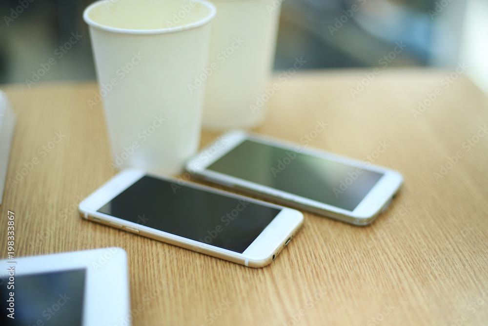 Two white mobile phones with tablet on wooden table background, blank screen electronic device with copy space. Two white mobile phones with tablet on wooden table background, blank screen electronic device with copy space.