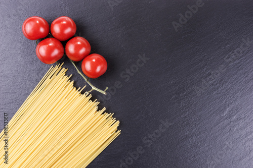 Yellow long raw spaghetti and cherry tomatoes on black slate plate