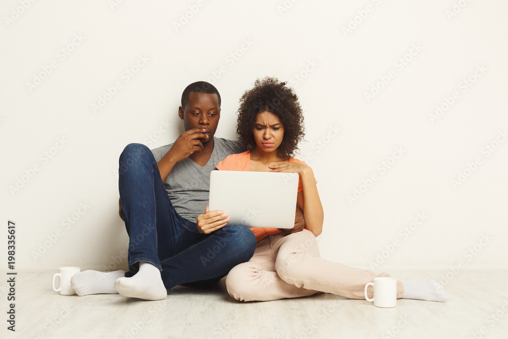 Shocked couple using laptop, sitting on floor Shocked couple using laptop, sitting on floor