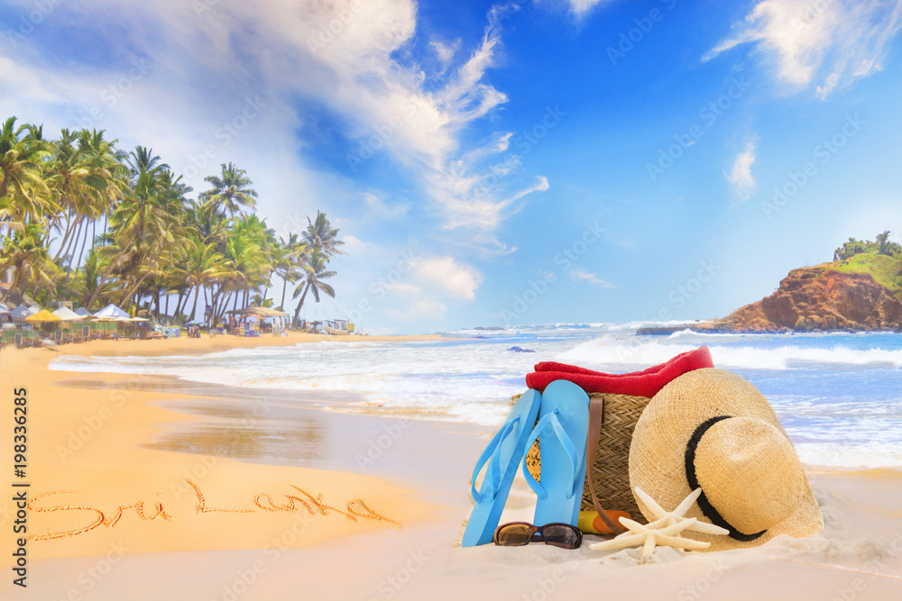 Straw hat, sunglasses, slippers and a bag on the golden sand of Sri Lanka's beach