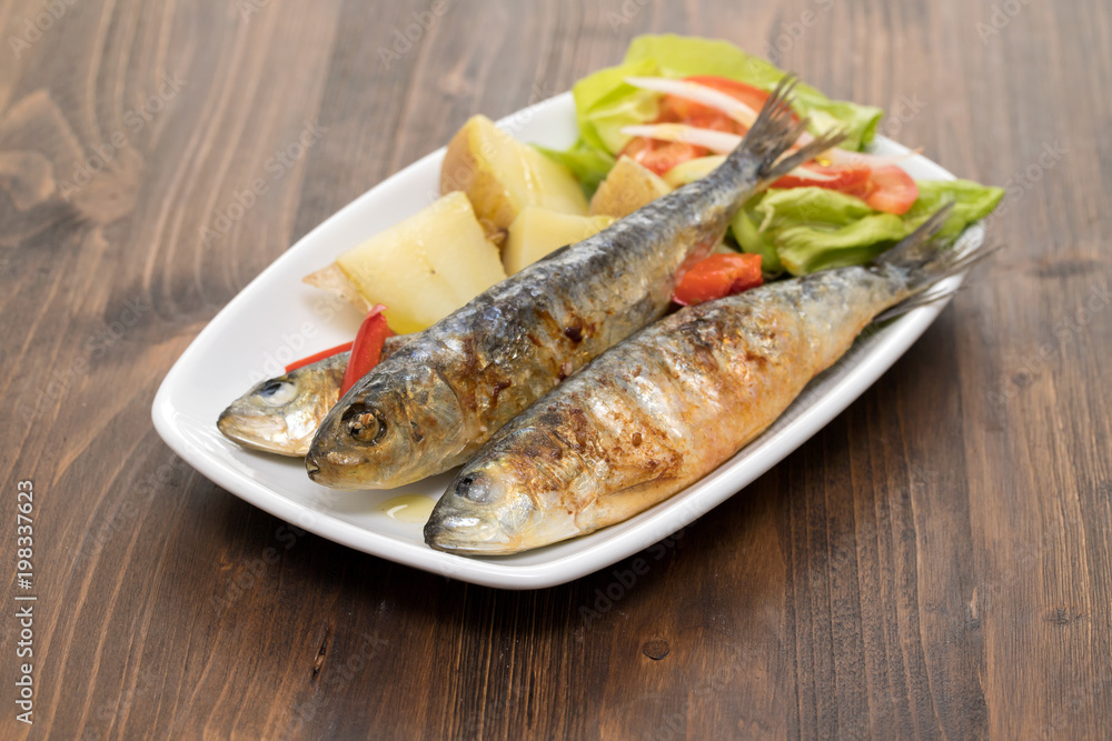 grilled sardines with boiled potato and salad on white plate grilled sardines with boiled potato and salad on white plate