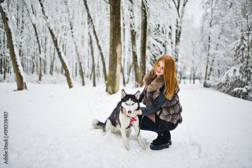 Red haired girl walking at park with husky dog on winter day.