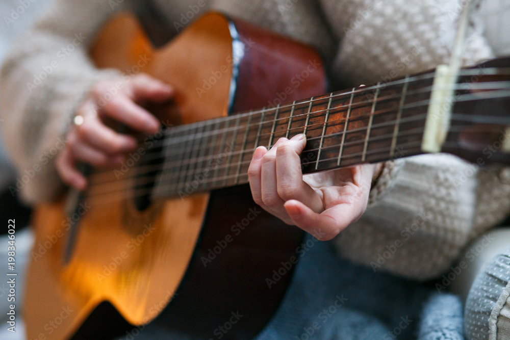 Play the guitar by hand Artist or musician.Young woman hands in knitted sweater. Home music party