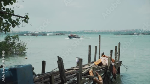 Slow motion long shot establishing shot of a bumboat filled with tourists crossing the Johor Strait towards Pulau Ubin island in Singapore photo