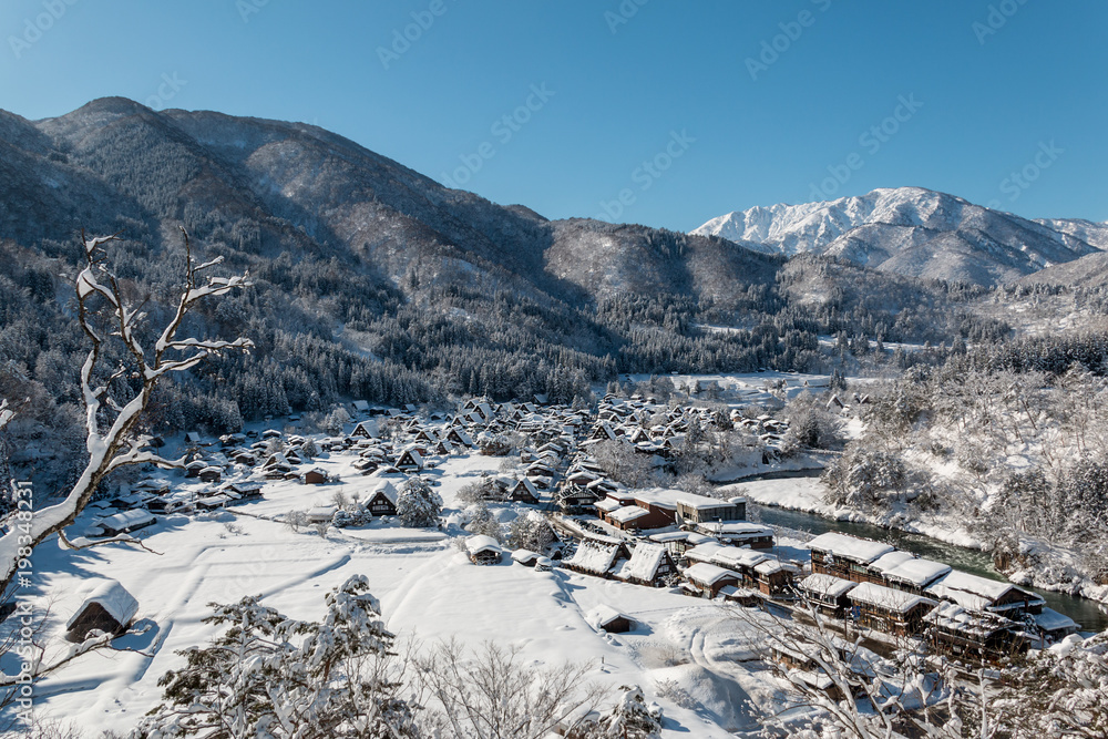 The panoramic viewpoint of Gassho houses in Shirakawago village with snow covered ground ,blue sky and mountains background at winter  in Gifu,Japan.
