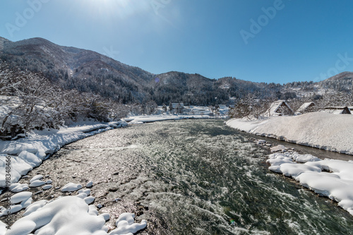 Shogawa river in Shirakawago village with snow covered ground ,blue sky and mountains background at winter in Gifu,Japan.