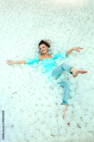 Happy beautiful woman lays surrounded by white plastic balls in the dry pool for adult. Copy space. photo