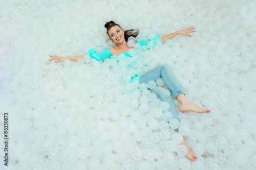 Happy beautiful woman lays surrounded by white plastic balls in the dry pool for adult. Copy space. photo