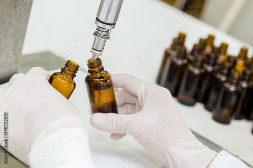 Close up of female lab worker hand with gloves filling the bottle with syrup