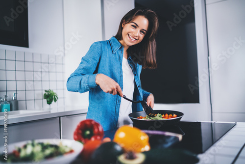 Obraz na plátně Happy smiling woman cooking in kitchen at home fresh vegetables, happy brunette