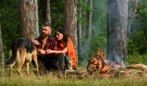 Couple play with german shepherd dog near bonfire, forest background.