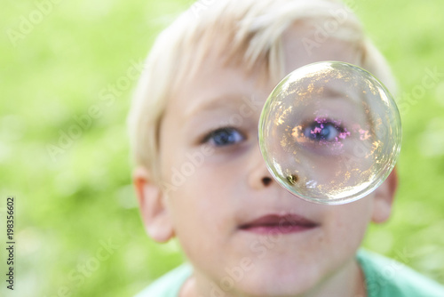 Young boy blowing bubbles with greenery background. Selective focus. 