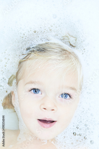 Happy little baby girl face swimming in the bathroomand smile. Portrait of baby bathing in a bath full of foam
 photo